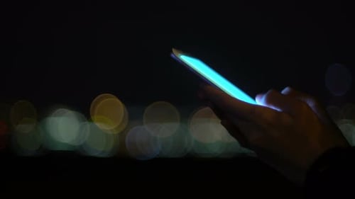 Hand Using Glowing Smartphone at Night, City Bokeh