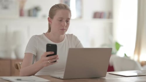 Beautiful Young Woman Using Smartphone While Using Laptop in Office