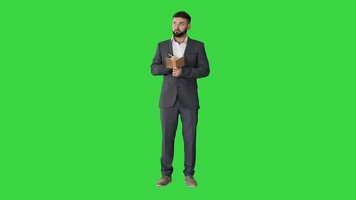 Concentrated Young Man in Formalwear Holding Note Pad and Writing on a Green Screen, Chroma Key