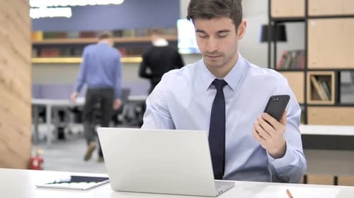 Man Using Mobile and Laptop in Modern Office