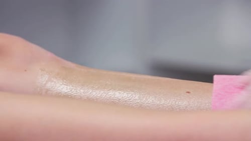 Waxing Master Depilating Woman's Legs Using Pink Waxing Strips