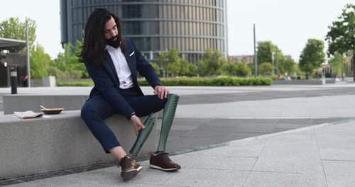 Business man adjusting his prosthetic leg outdoor from office building - Job and insurance concept
