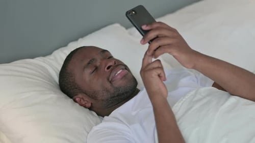 Young Adult Using Mobile Phone While Lying in Bed