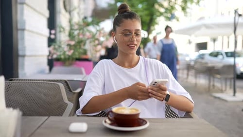 Beautiful Young Woman Sitting in Street Cafe Using a Smartphone