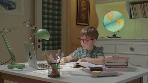 Elementary Age Boy Writing Down in Notebook and Showing to Online Teacher