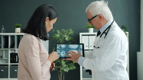 Sick Woman Looking at MRI Images on Tablet Screen During Doctor Appointment in Clinic