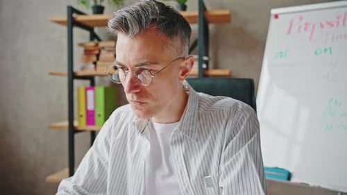 Concentrated Middle Aged Man in Eyeglasses Typing on Laptop Computer Working at Home Office Zoom Out