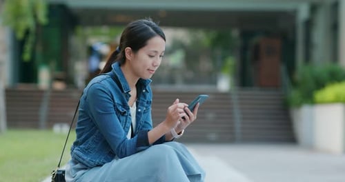 Woman Uses Phone Sitting Outdoors on Sunny Day