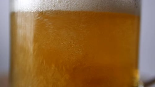 Close-up Shot of Light Beer Is Poured Into a Beer Glass with a Handle, a Lot of Bubbles and Foam