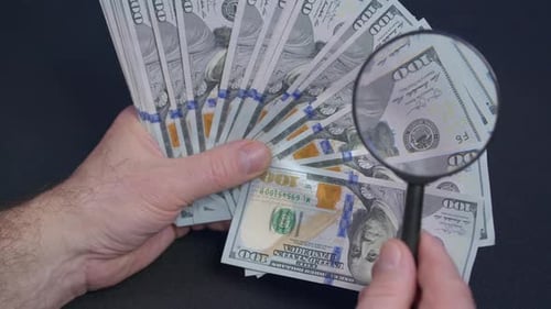 Person Checking Dollar Banknote for Authenticity with Magnifying Glass Close Up
