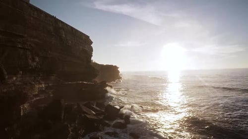 Epic aerial drone view of a cliff at sunset over a village near Lisbon while the waves splash again