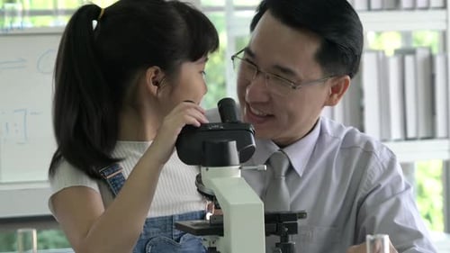 Girl and Man Look into a Microscope