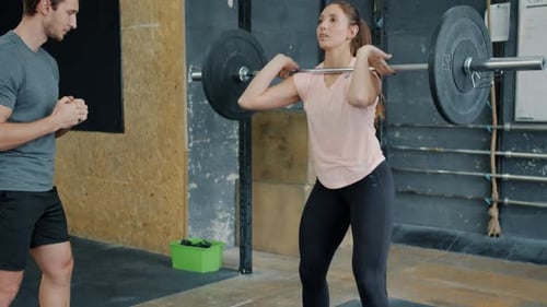 Young Sportswoman Squatting with Barbell Weightlifting Working Out in Gym with Coach