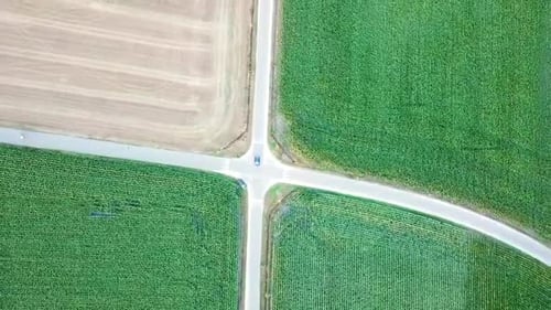 Un solo coche conduciendo en una encrucijada con campos verdes, helicóptero Zumbido vista perfecta plaza más sha