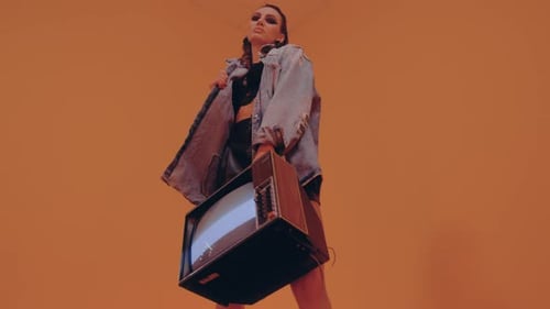 Stylish Woman Holding Retro Television in Orange Studio
