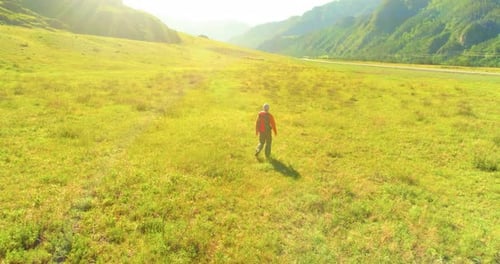 Flight Over Backpack Hiking Tourist Walking Across Green Mountain Field. Huge Rural Valley at Summer