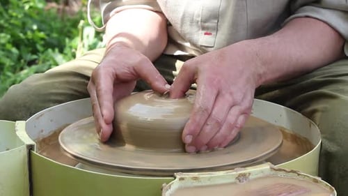 Male Potter of Caucasian Ethnicity in Working Uniform Makes a Small Clay Pot