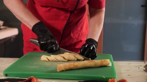Cook Hands Cutting Thin Pancake Roll on Kitchen Board with Knife