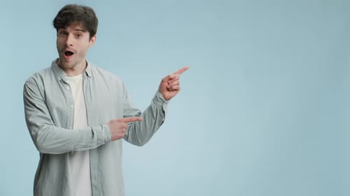 Young Emotional Man Looking Aside and Seeing Surprising Advertisement Pointing Aside at Empty Space