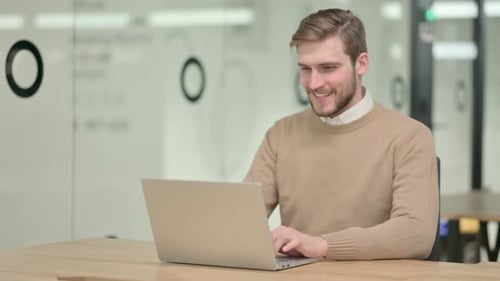 Man Video Calling on Laptop in Office Waving