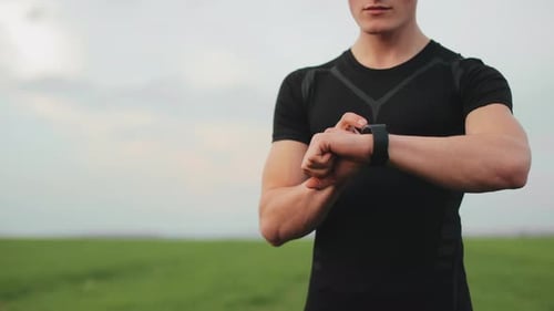 Man Checks Smart Watch in Green Field
