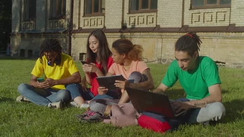 College Students Using Devices on Grassy Campus