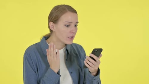 Woman Reacting to Smartphone Content Against Yellow Background