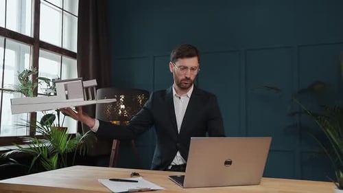 Male Designer in Office Working on Laptop with Model House.