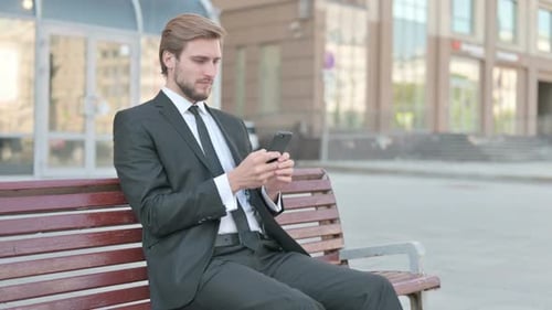 Man in Suit Using Phone on City Bench