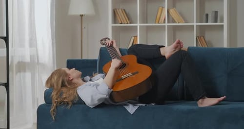 Woman Lies on Couch Playing Acoustic Guitar