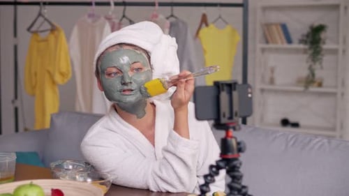 A Girl With a White Towel Put on Her Face a Green Mask During Blogging