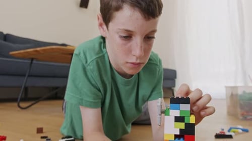Boy Concentrates Building with Multicolored Blocks Indoors