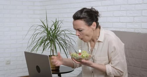 Adult Eats Salad While Using Laptop at Home