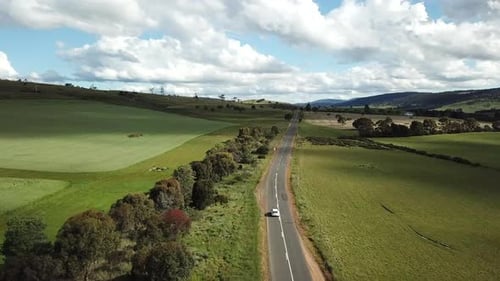 Vue par drone d'une voiture conduisant au loin le long d'une route de campagne bordée d'arbres et de champs