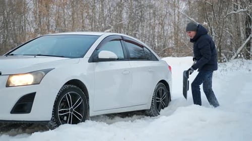 Man shovels snow away from car in winter