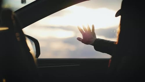 Woman in Car Watching Sunset With Hand Up