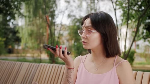 Woman Using Phone on Bench in Urban Park
