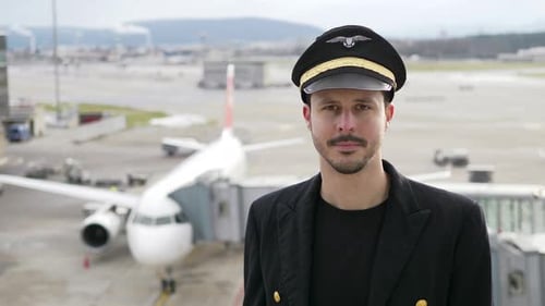 Pilot in Uniform Stands Before Airplane at Airport