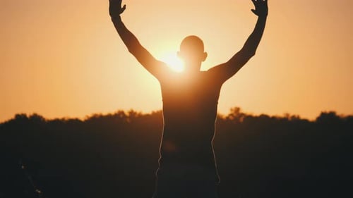 Silhouette of Man Against Sunset Raising Hands To Sides and Up. Slow Motion