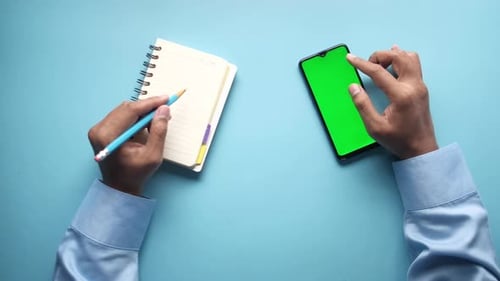 Menschenhand mit Smartphone und Schreiben auf Notizblock