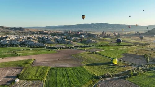 Hot air balloons fly over the mountainous landscape of Cappadocia, Turkey.