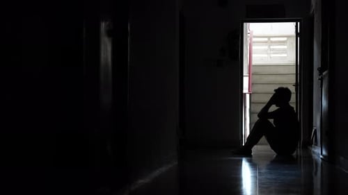 Silhouetted Adult Sitting Head in Hand Dark Hallway