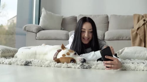 Woman Using Phone While Lying with Dog