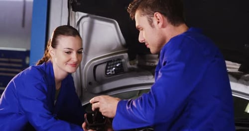 Male mechanic checking a car parts while female mechanic servicing a car