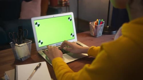 Beautiful Black Woman Sitting at Her Desk Works on a Laptop with Green Chroma Key Mockup Screen