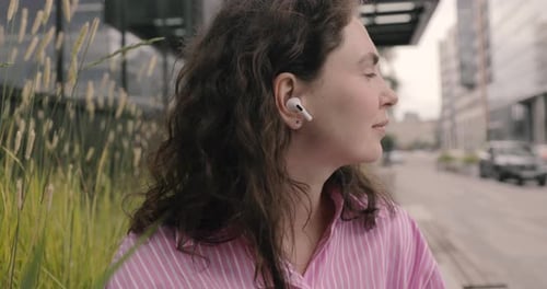 Young Woman Listens to Earbuds Outdoors in City