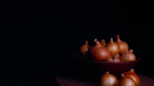Pile of whole bulbs of raw onion in ceramic bowl on table.
