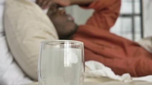 Un homme noir afro-américain est allongé dans son lit avec une forte fièvre et prend des antipyrétiques