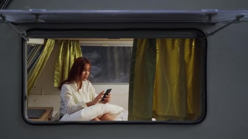 Woman Using Mobile Phone in Caravan Bed