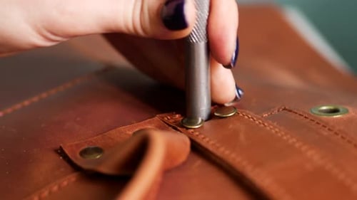 Craftsperson Secures Leather Fasteners with Metal Tool